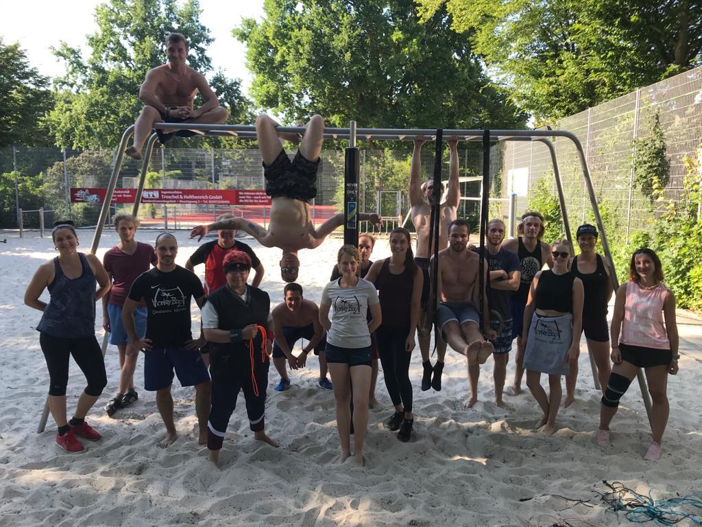 Gruppenzusammenkunft von 20 Personen auf einem Sandplatz, posierend an einem Spielgerät im Freien.