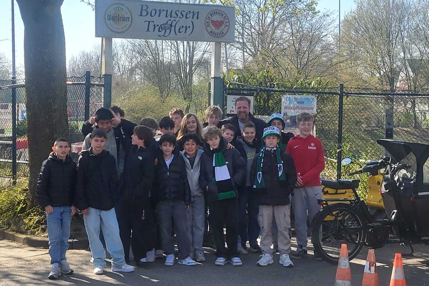 Gruppe von Jugendlichen steht vor dem „Borussen Treff“ mit einem Fahrrad und Verkehrskegeln im Vordergrund.