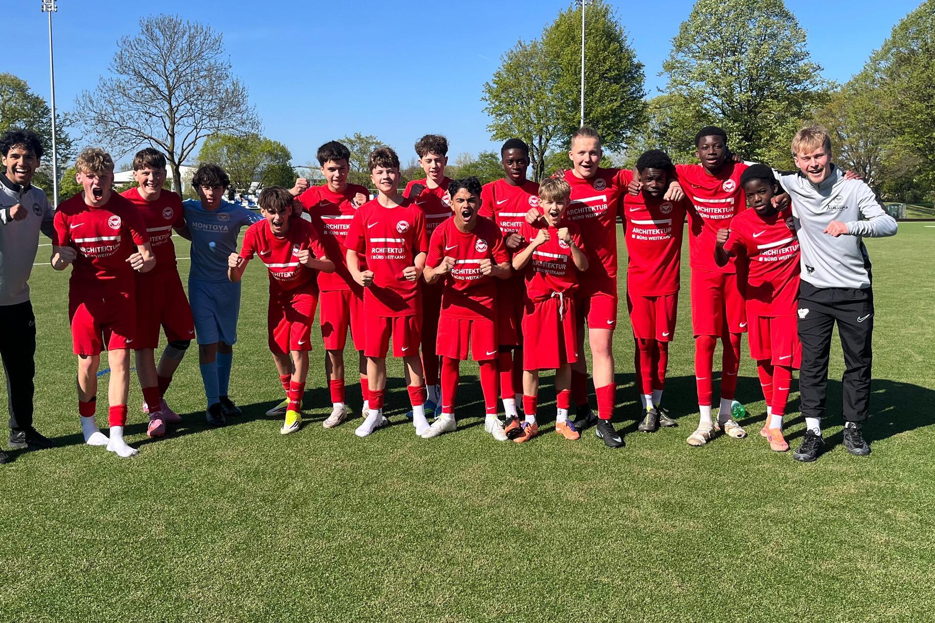 Gruppe junger Fußballspieler in roten Trikots posiert auf einem grünen Feld unter blauem Himmel.