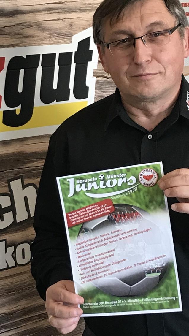 Mann hält ein Informationsblatt über die Jugendabteilung von Borussia Mönster vor einer Werbewand.