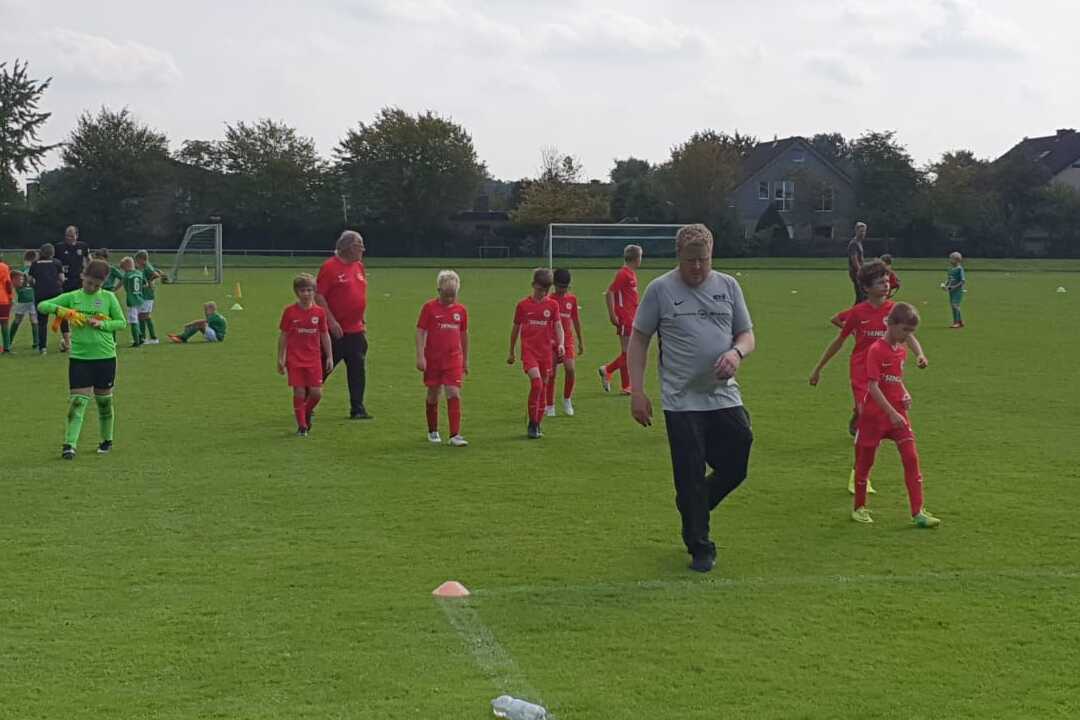 Fußballmannschaft in roten Trikots joggt auf einem grünen Spielfeld, während Trainer sie anleitet.