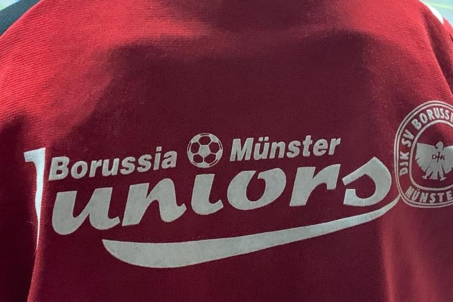 Rückansicht eines roten T-Shirts mit dem Aufdruck „Borussia Münster Juniors“ und Vereinslogo.