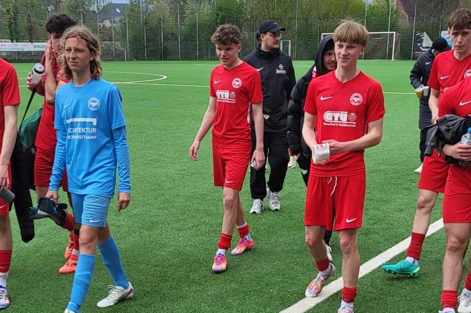 Gruppe junger Fußballspieler in roten Trikots verlässt das Spielfeld, begleitet von einem Trainer in schwarzer Kleidung.