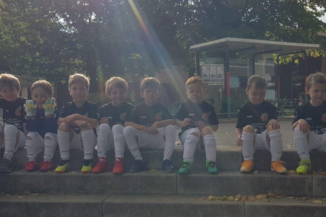 Gruppe von Kindern im Sportoutfit sitzt auf Treppenstufen in einem Außenbereich, mit Bäumen im Hintergrund.