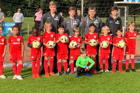 Gruppe von Fußballspielern in roten Trikots steht vor einem Tor, umgeben von einem Sportplatz und Zuschauern.