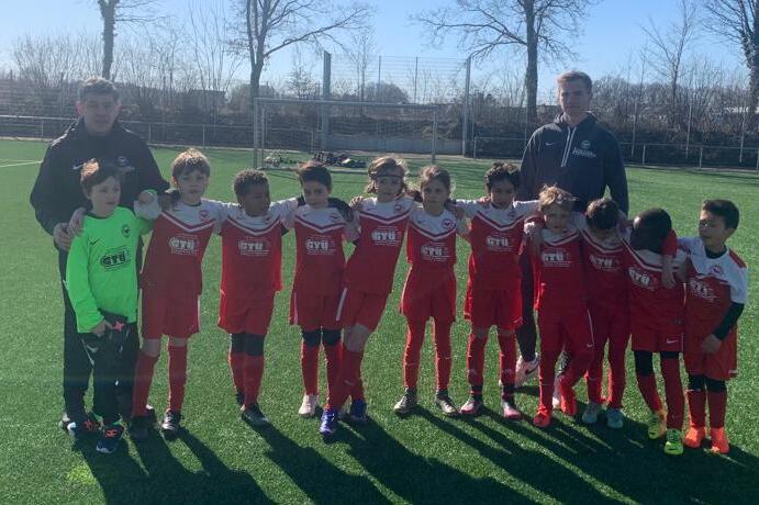 Eine Gruppe von elf jungen Fußballspielern in roten Trikots posiert auf einem Rasenplatz mit zwei Trainern.