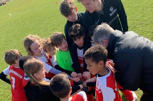 Gruppierung von Kindern in Fußballtrikots um einen Trainer, während sie sich zum Team-Motivationsruf versammeln.