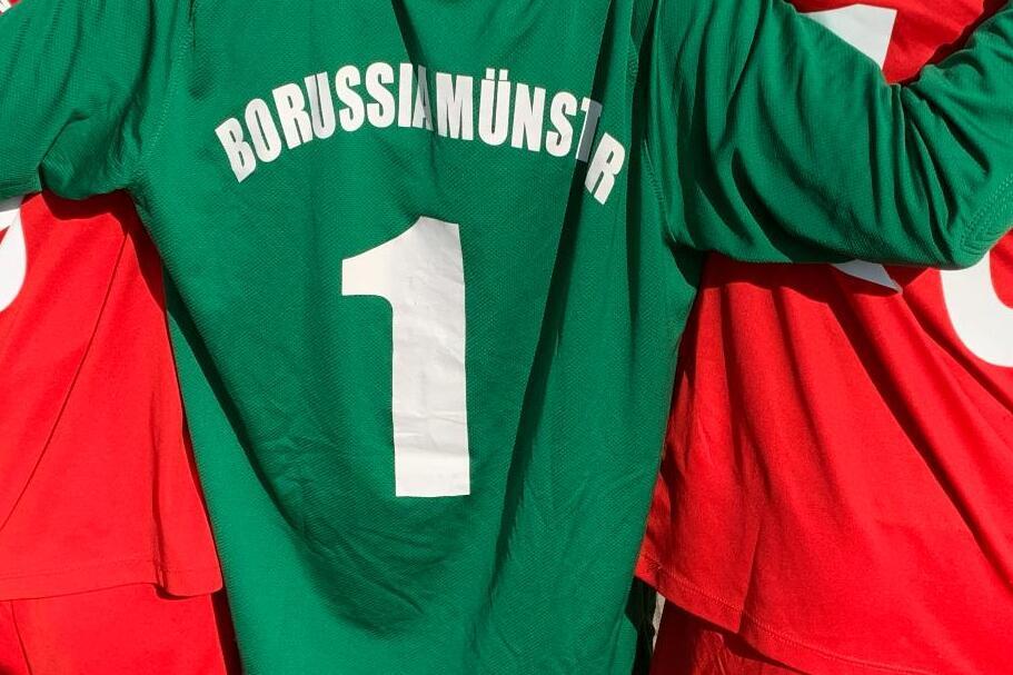 Nahaufnahme von drei Fußballspielern: einer in grünem Trikot mit „BORUSSIAMÜNSTER“ und zwei in roten Trikots.
