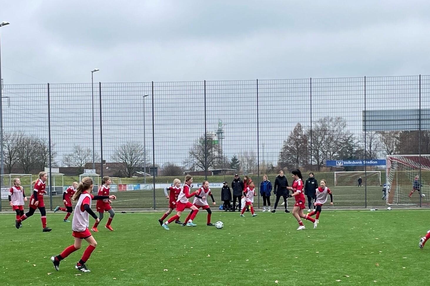Mannschaftssport auf einem Fußballplatz mit mehreren Spielerinnen in roten Trikots, die um den Ball kämpfen.