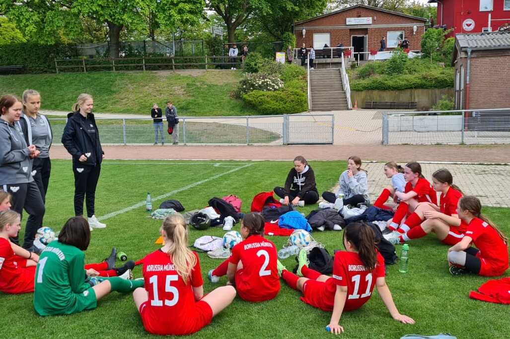 Gruppe von Mädchen in roten Trikots sitzt auf einem Fußballfeld und unterhält sich in Teamformation.