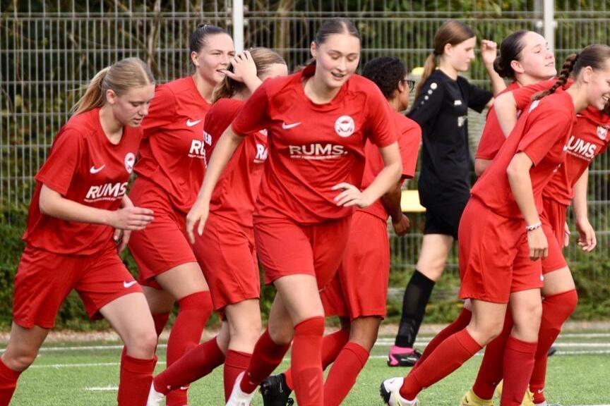 Mannschaft von Frauen in roten Trikots beim Aufwärmen auf einem Fußballfeld.