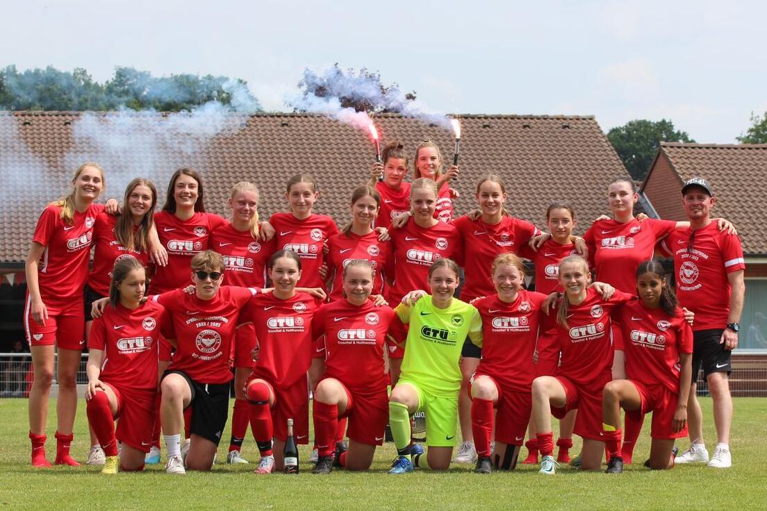 Gruppenfoto einer Fußballmannschaft in roten Trikots, versammelt auf einem Platz mit Rauchfackeln im Hintergrund.