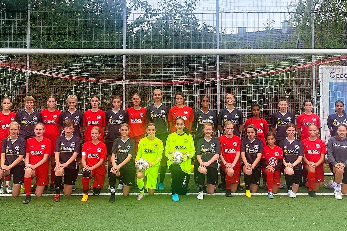 Gruppenfoto einer Mädchenfußballmannschaft, bestehend aus 24 Spielerinnen in roten und schwarzen Trikots, vor einem Tor.