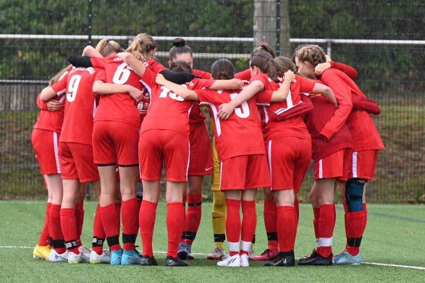 Eine Gruppe von 12 Fußballspielerinnen in roten Trikots steht im Kreis und hält sich an den Schultern.