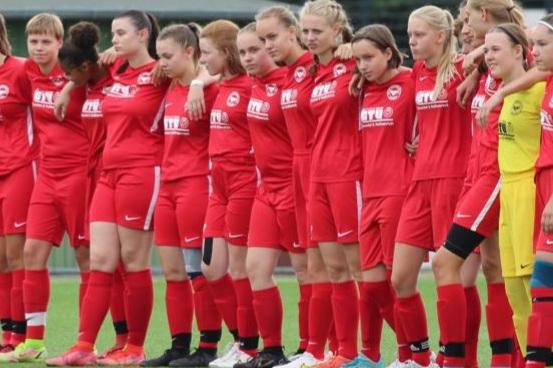 Gruppenszene von Frauenfußballerinnen in roten Trikots, auf einem Spielfeld, stehen nebeneinander vor einem Spiel.