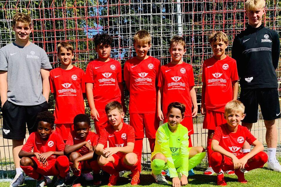 Gruppe von zehn jungen Fußballspielern in roten Trikots, posierend vor einem Fußballtor auf einem grünen Platz.