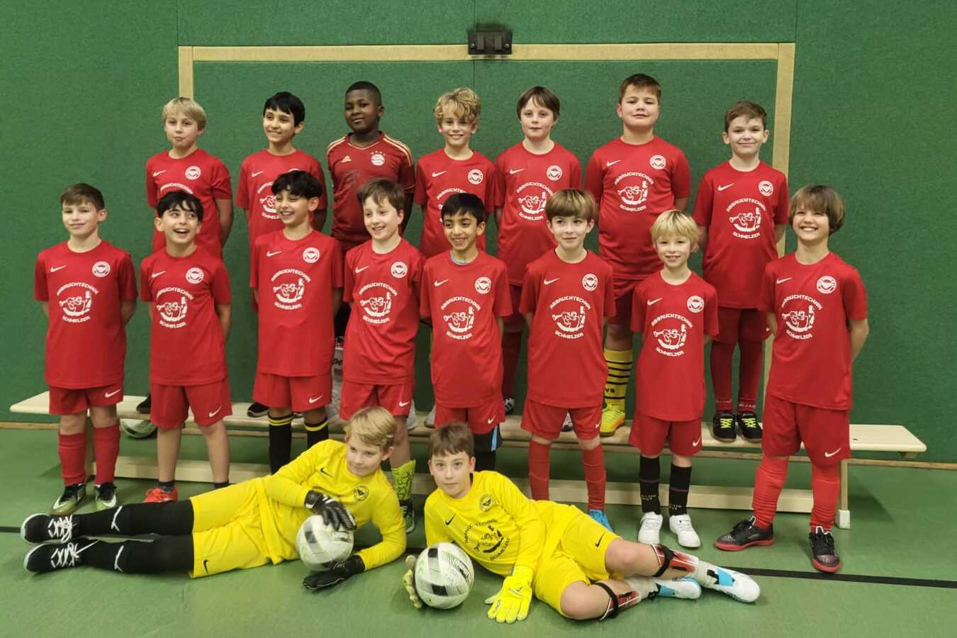 Gruppenupload von jungen Fußballspielern in roten Trikots, inklusive Torwart im gelben Trikot, vor einem Tor.
