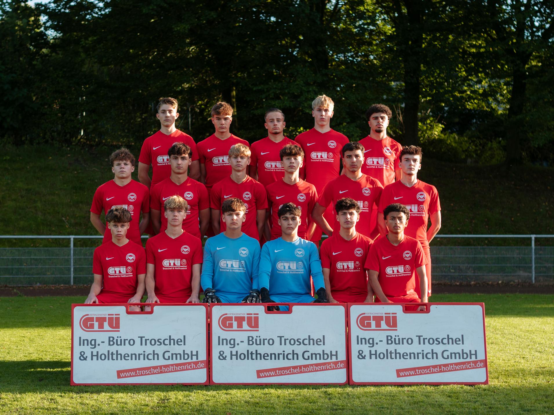 Mannschaftsfoto einer Jugendfußballmannschaft in roten Trikots mit Torwart, zwei Sponsorenbannern im Vordergrund.