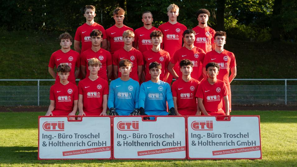 Mannschaftsfoto einer Jugendfußballmannschaft in roten Trikots mit Torwart, zwei Sponsorenbannern im Vordergrund.