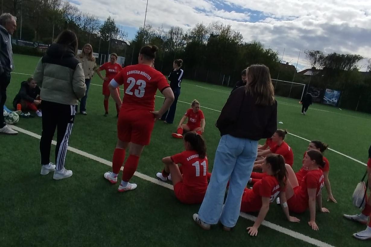 Gruppe von Fußballspielerinnen in roten Trikots auf dem Rasenplatz, während sie sich nach dem Spiel versammeln.