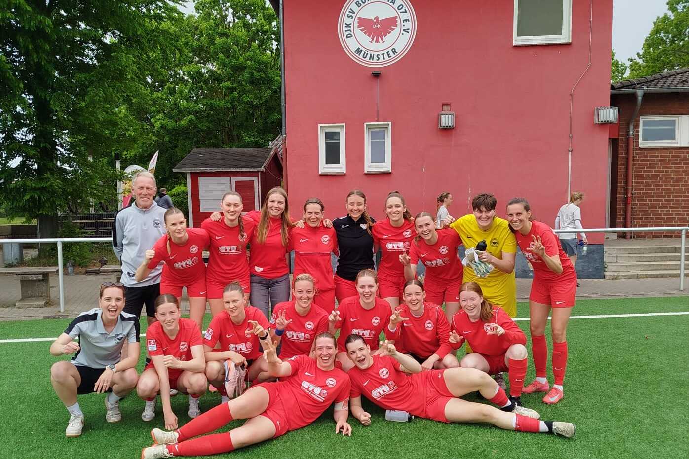 Gruppenshot eines Frauenfußballteams in roten Trikots vor einem Vereinsgebäude, einige Spielerinnen liegen am Boden.