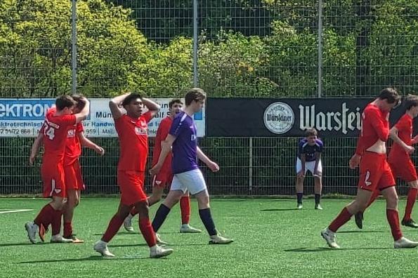 Fünf Fußballspieler in roten Trikots gehen auf einem Kunstrasenplatz, im Hintergrund ein Torwart in lila Trikot.