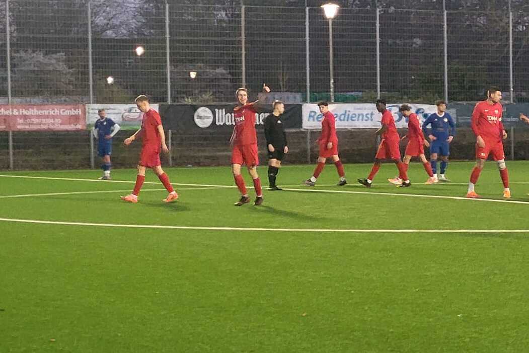Fußballspiel auf Kunstrasen mit Spielern in roten und blauen Trikots, umgeben von einer nächtlichen Umgebung.