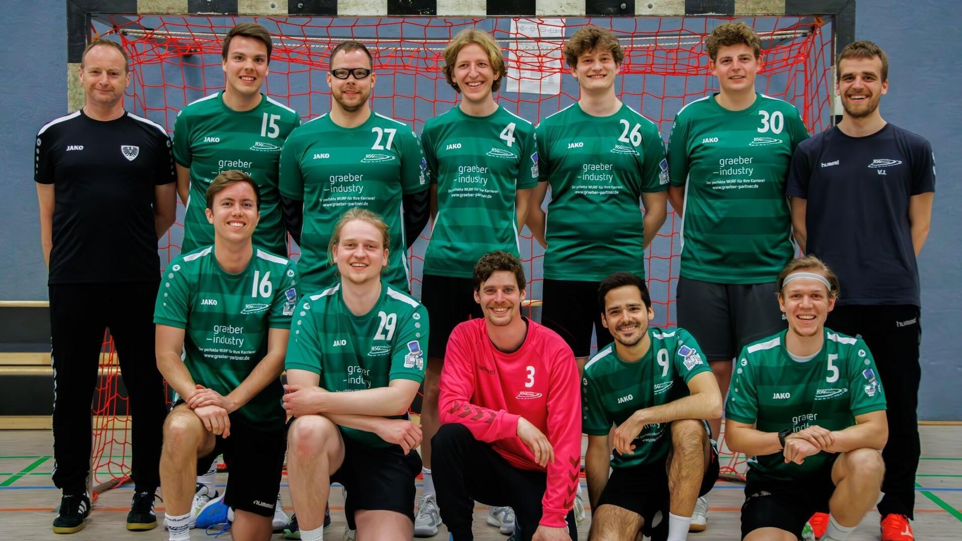 Mannschaftsfoto einer Handballmannschaft in grünen Trikots vor einem roten Tor.