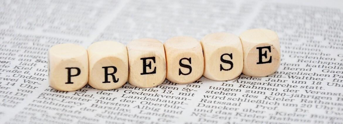 Buchstabenwürfel mit der Aufschrift „PRESSE“ auf einer bedruckten Zeitungsseite.